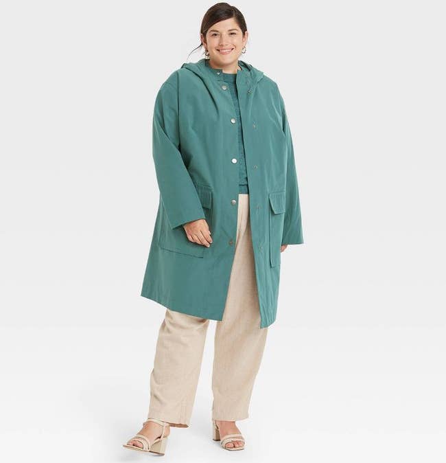 model in a thigh-length teal raincoat with a hood and large pockets
