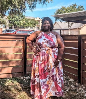 reviewer in patterned maxi dress stands smiling in a sunny outdoor area
