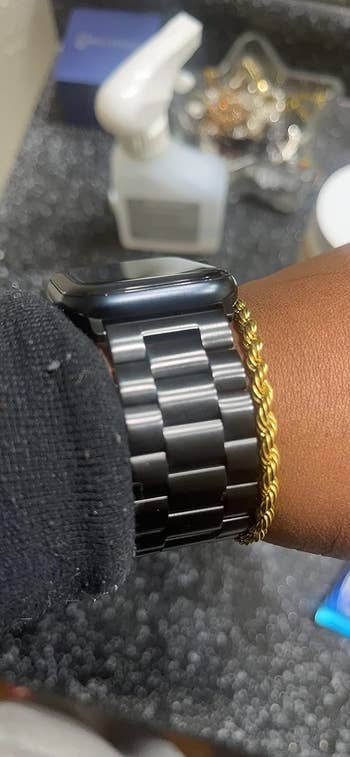 Reviewer with apple watch band in the color black on wrist with a thing gold chain bracelet