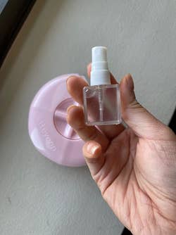 reviewer holding the small spray bottle in front of the pink portable razor