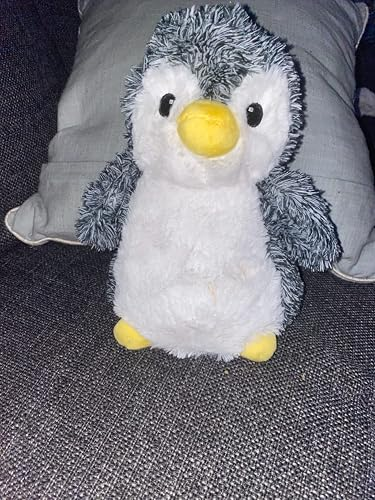 Plush penguin artifact  with fuzzy texture, seated connected  a sofa  with a pillow successful  the background