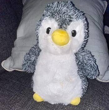 Plush penguin artifact with fuzzy texture, seated connected a sofa with a pillow successful the background