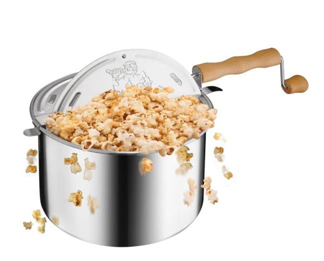 A metallic popcorn popper with popcorn flying out of it. 