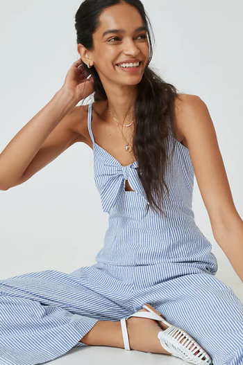 a model in a light blue pinstripe jumpsuit with thin straps and a bow in the chest area