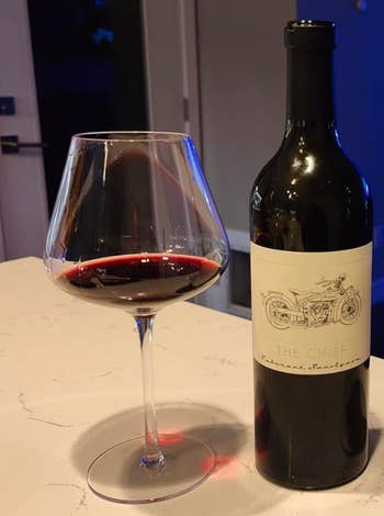 A deep stemmed wine glass with a wide-mouthed rim holding red wine 