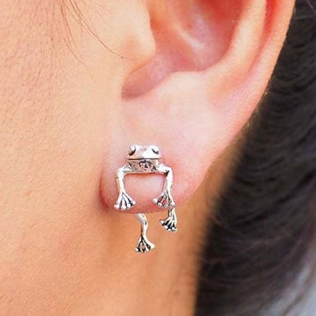 Close-up of a person's ear wearing a frog-shaped earring that clasps around the earlobe, suitable for adding a unique touch to an outfit