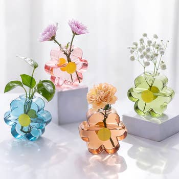 Flower-shaped solid vases successful pink, green, blue, and orangish with flowers, displayed connected achromatic pedestals
