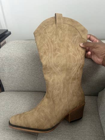 Person holding a knee-high cowboy footwear  with intricate stitching, placed connected  a couch