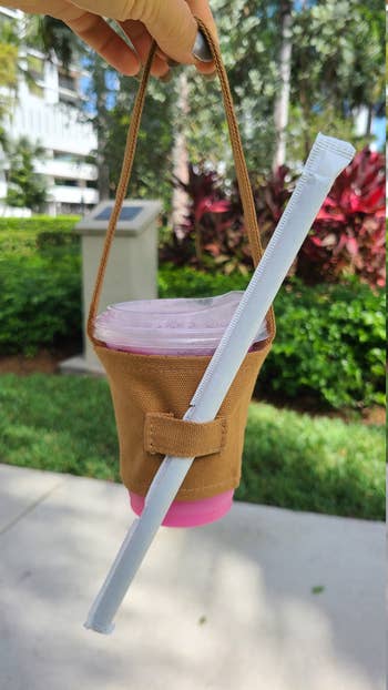 Reusable cup holder carrying a drink with a straw and lid, shown on a sunny day outdoors