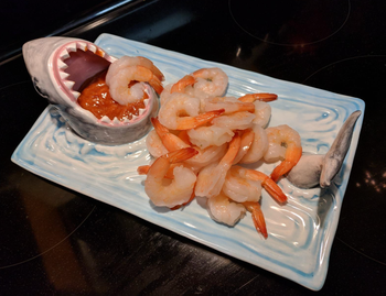 rectangular tray with shark tail on one side and open mouth filled with cocktail sauce on the other. reviewer filled tray with shrimp.