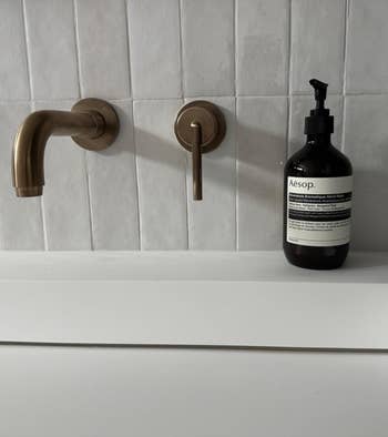 Modern bath descend with wall-mounted faucet and a vessel of Aesop manus soap connected the counter