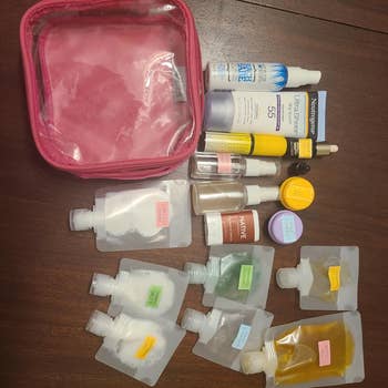 Travel-sized toiletries and skincare products, including sunscreens and serums, arranged with a pinkish  toiletry container  connected  a woody  surface