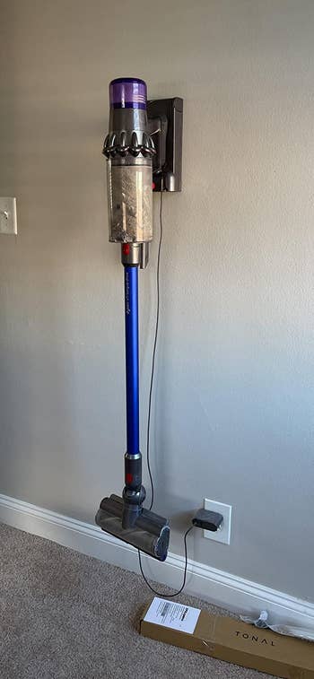 reviewer image of the dyson vacuum hanging from a wall mounted charger