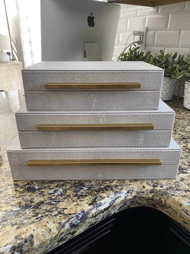 Three faux-leather boxes stacked on a granite counter in descending order