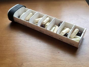 reviewer's opened pill organizer with compartments for each day of the week, filled with various pills