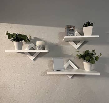 Reviewer image of three white floating shelves wit rhombus-shaped mounts and plants on top of each 