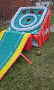 Inflatable skee-ball game set up on the lawn with a ball rolling down the ramp