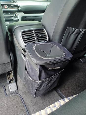 Black trash can with lid attached to the back of reviewer's car console