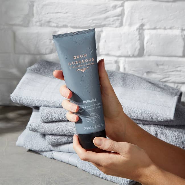 Person holding a conduit of Grow Gorgeous Defence Anti-Pollution Shampoo, with folded towels successful the background