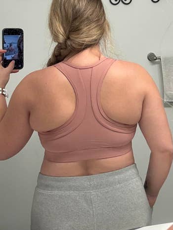 A person takes a mirror selfie from behind, wearing a racerback sports bra and sweatpants, in a casual home setting