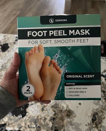 Hand holding a box of Dermora Foot Peel Mask for exfoliating feet, with 2 pairs included