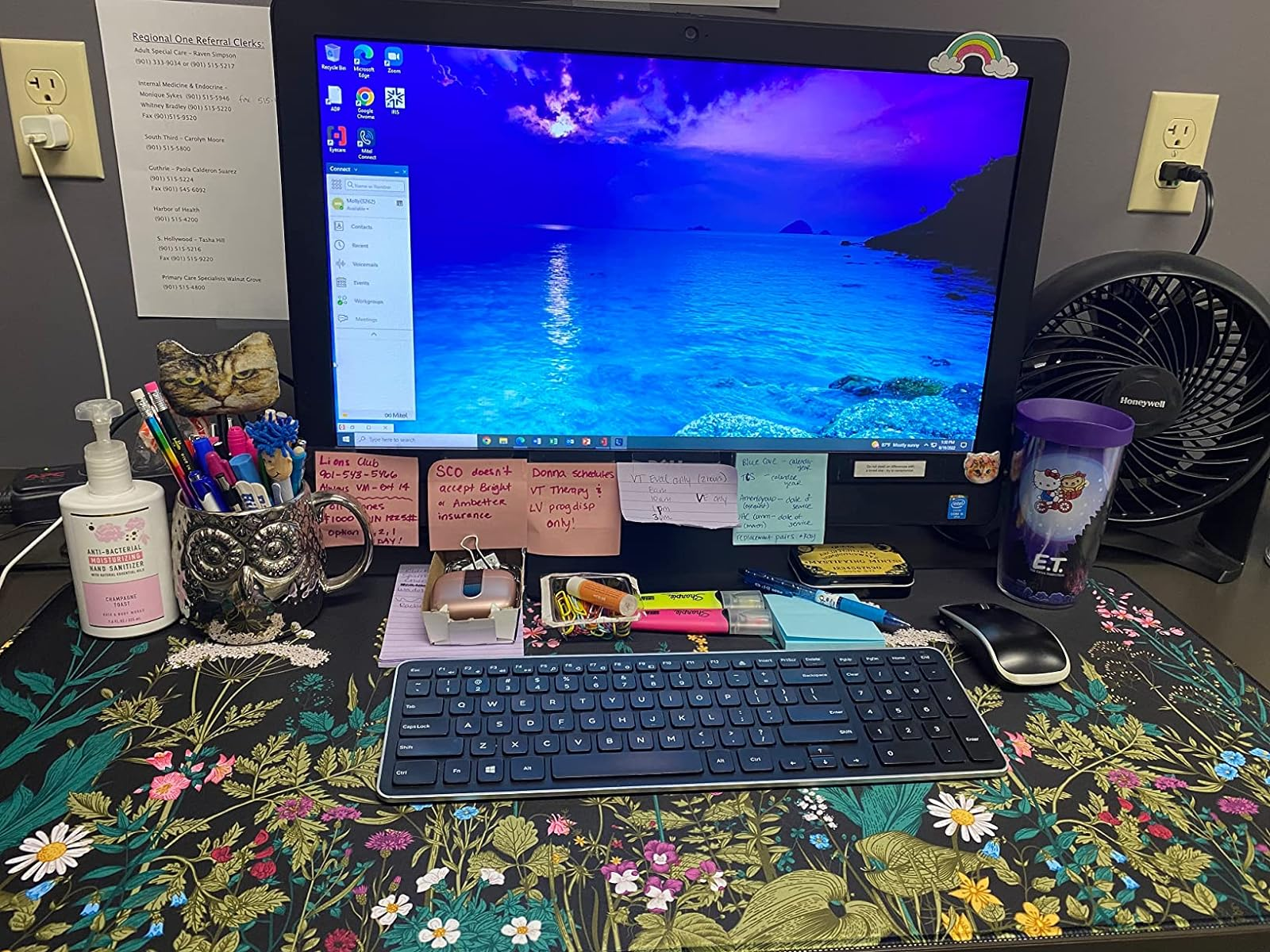 Desk with computer on a black desk mat with a multicolor floral print 