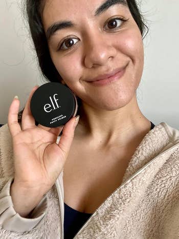 Woman holding a compact of e.l.f. cosmetics, smiling, in casual attire