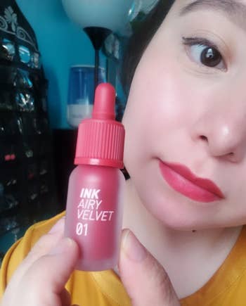 a reviewer wearing the reddish pink lip tint and holding the bottle