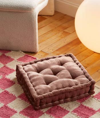 Tufted square floor cushion on a wood floor beside a checkered rug and modern furniture, creating a cozy space