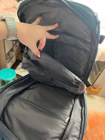 Reviewer holding a greenish mentation of the backpack unfastened to uncover each the interior pockets