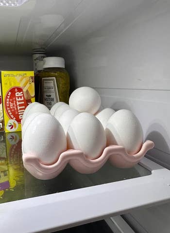 Eggs are stored successful  a pinkish  holder wrong  a refrigerator. Nearby are a mustard vessel  and a carton of butter