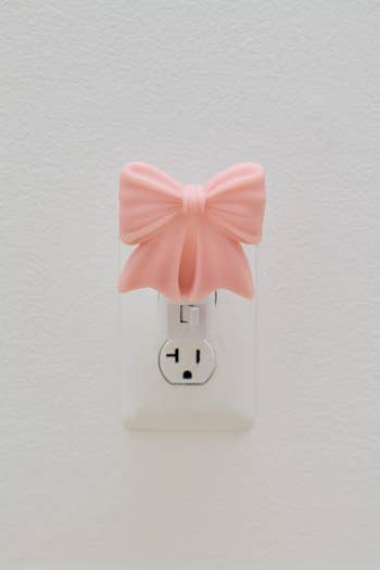 Power outlet plug covered with a decorative pink bow adapter, adding a stylish touch to a typical wall socket