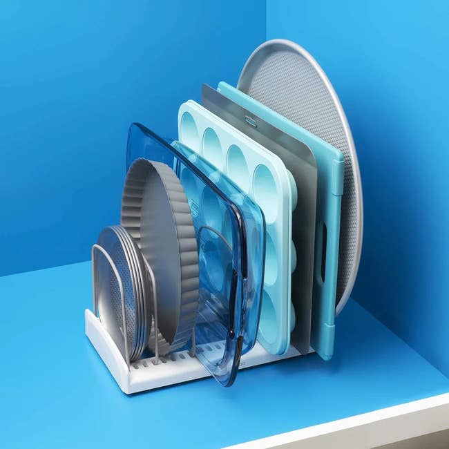 Bakeware organized in a white rack on a blue countertop, featuring muffin trays, round pans, and a baking sheet neatly stacked