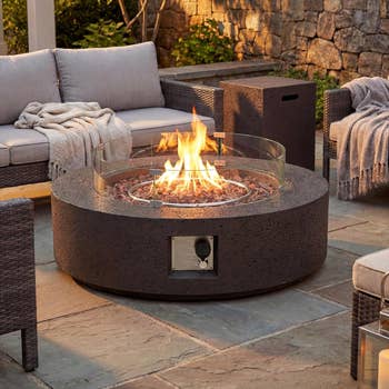Outdoor fire pit on a patio surrounded by wicker seating with cushions and blankets