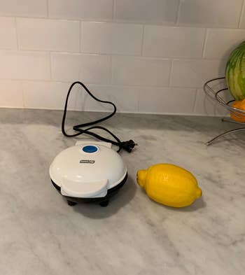 reviewer image of the small waffle maker in white, next to a lemon, showing the small size
