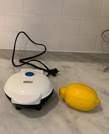 reviewer image of the small waffle maker in white, next to a lemon, showing the small size