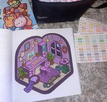 Markers in a case, a guide, and open book with a playful, cartoonish room design featuring a cozy reading nook with plants and décor on a fluffy surface