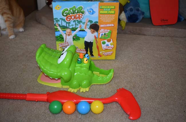 Gator Golf game set with an alligator target, colorful balls, and a red putter. The box shows children playing. Background includes Disney-branded item