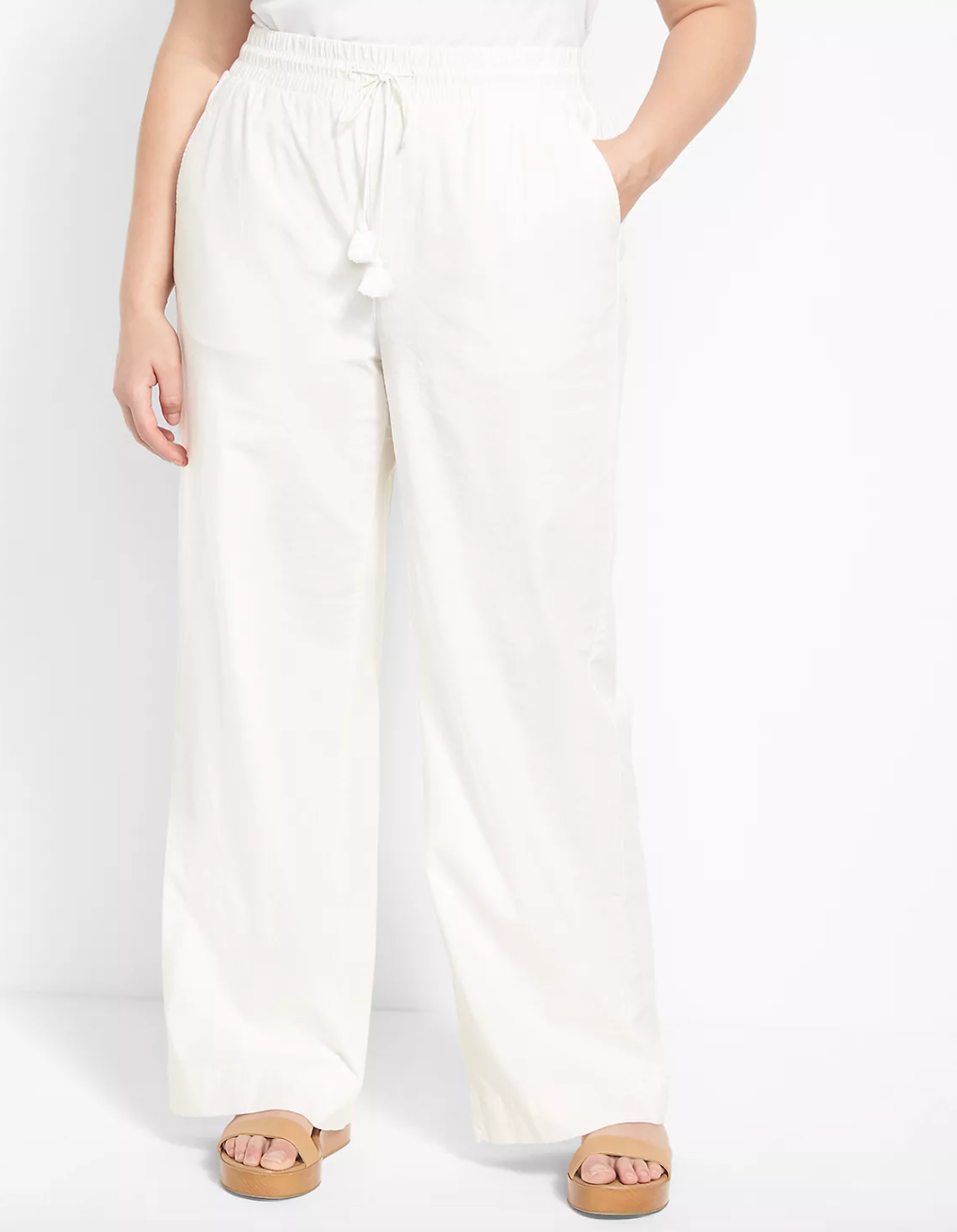 Model is wearing white linen pants and tan platform sandals