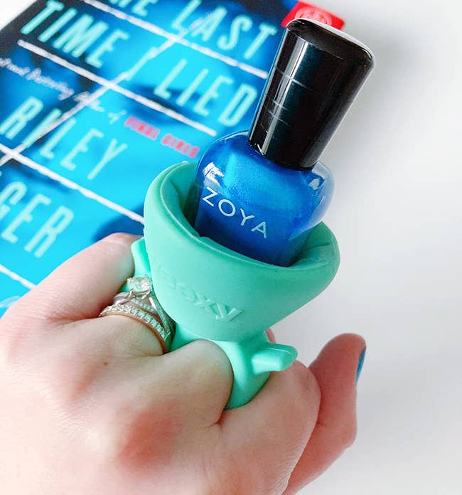 reviewer wearing the teal nail polish ring that's holding a bottle of blue nail polish