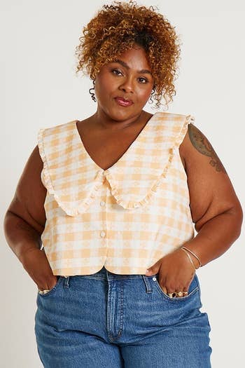 Woman in a checkered ruffle sleeveless top and jeans, posing for a fashion article