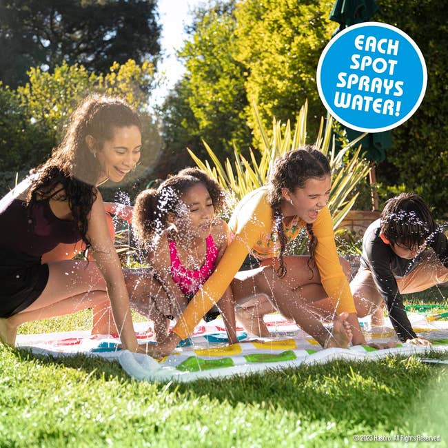 Four people playing on a wet outdoor Twister game mat with water spray feature