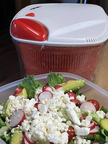 the red and white salad spinner next to a prepped salad