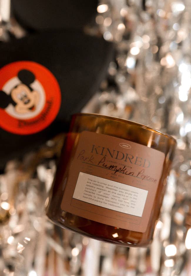 pumpkin park popcorn candle laying on silver confetti with a mickey hat laying in the background