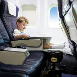 child model using the suitcase as a foot rest on an airplane
