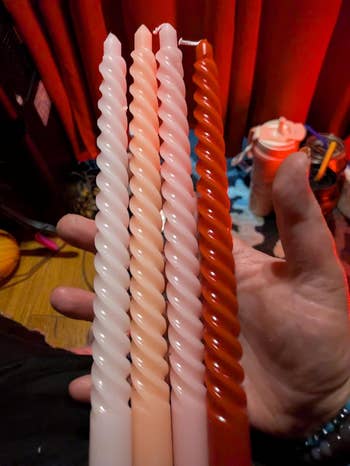 Four spiral candles held successful  a hand, each   with antithetic  shades. Background includes tiny  objects and curtains, suggesting an indoor setting