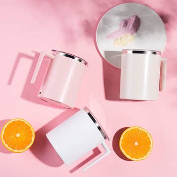 three of the mugs in assorted colors next to orange slices and a plate filled with different powders on a pink background