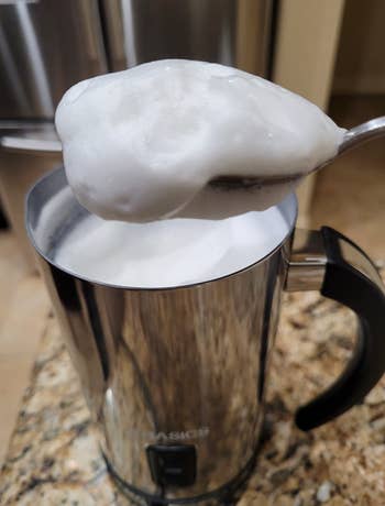 silver frother with a spoon dipped into it to show frothed milk 