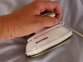 A hand holding a compact clothes steamer over a piece of fabric