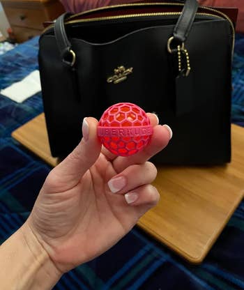 Hand holding a pink reusable sticky ball in front of a black handbag